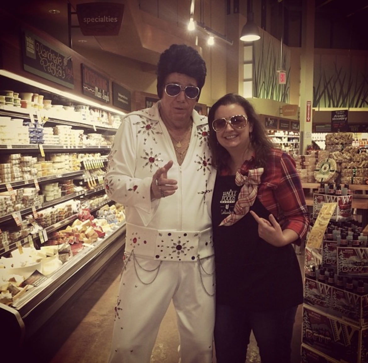 Kathleen in a Whole Foods apron beside an Elvis impersonator in the specialty cheese aisle