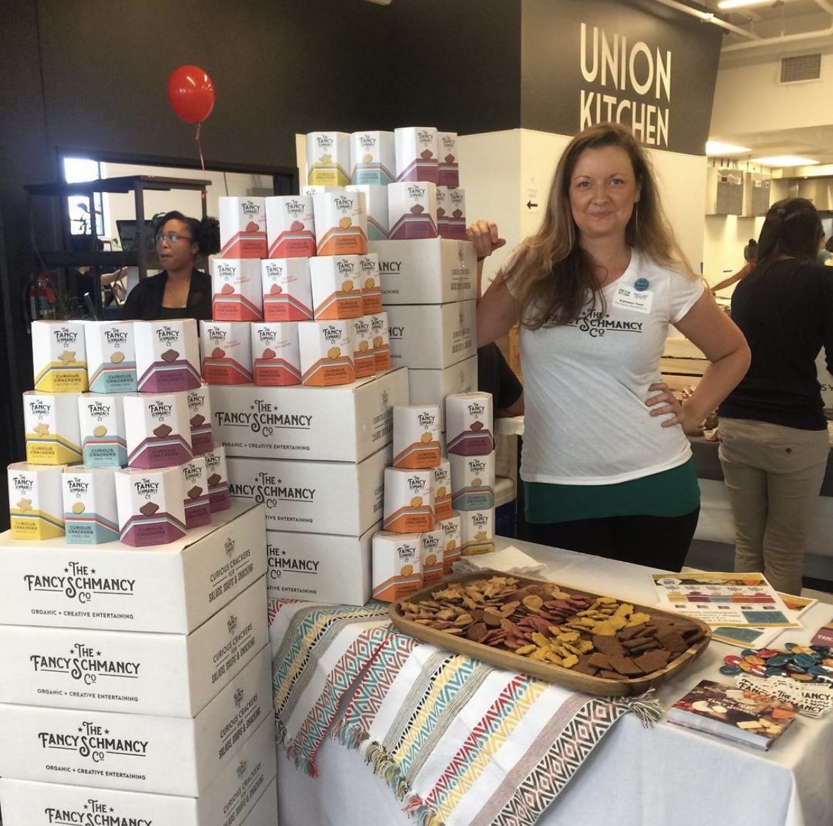 Kathleen beside towering pyramids of custom hexagonal Fancy Schmancy retail boxes and shipping cases
